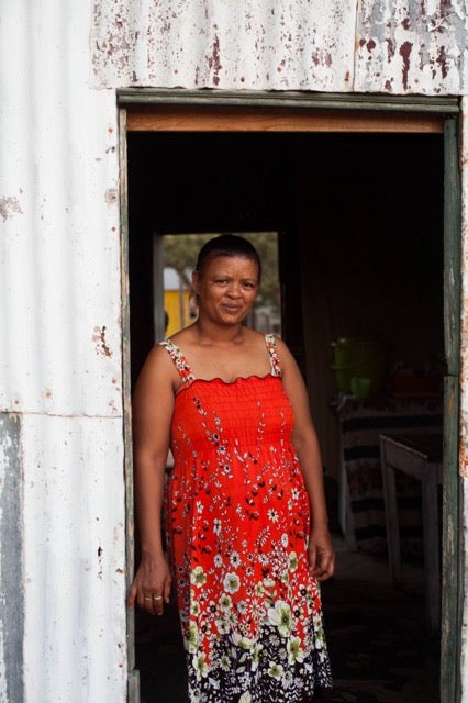 Nama woman standing in the doorway to her home in Kuboes, South Africa, wearing red dress