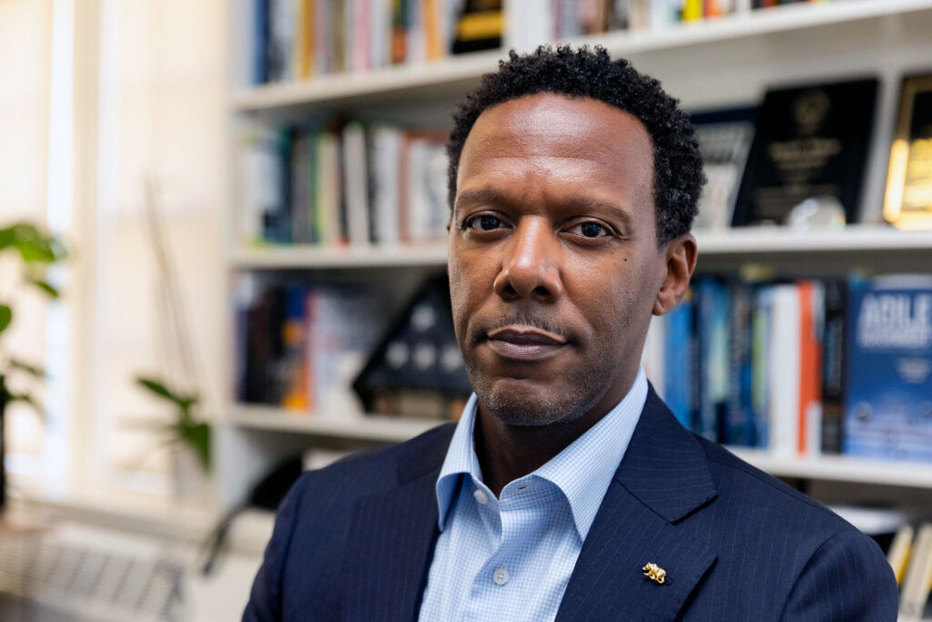 David C Wilson looks at the camera in his office, wearing a blue suit jacket and a faint smile