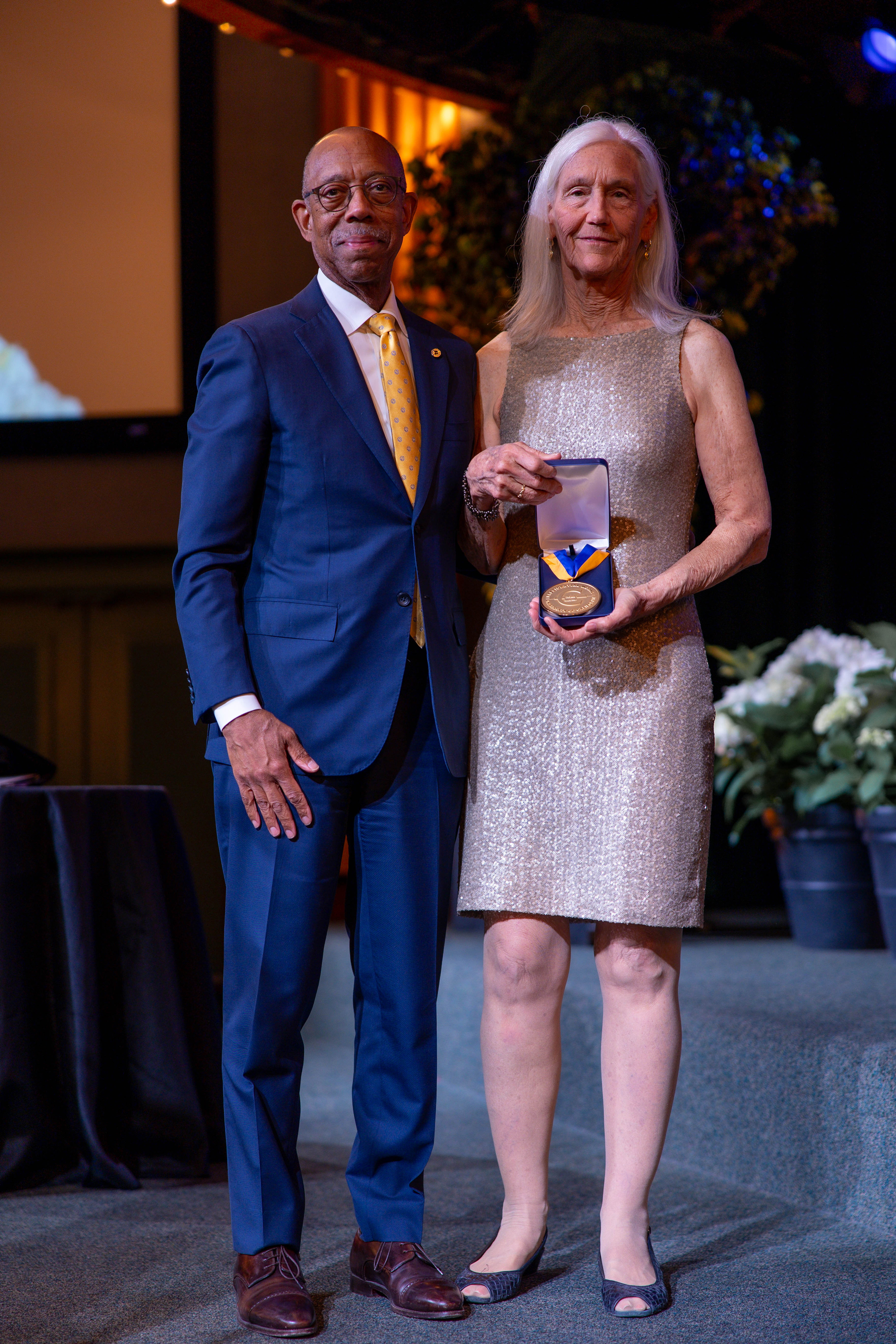 President Drake, left, in a blue suit and orange tie, next to Julie Packard, right, holding the UC Presidential medal