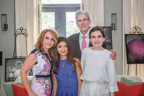 Woman in floral dress next to two pre-teen daughters, Dr. Frenk standing behind, in the Frenk family living room