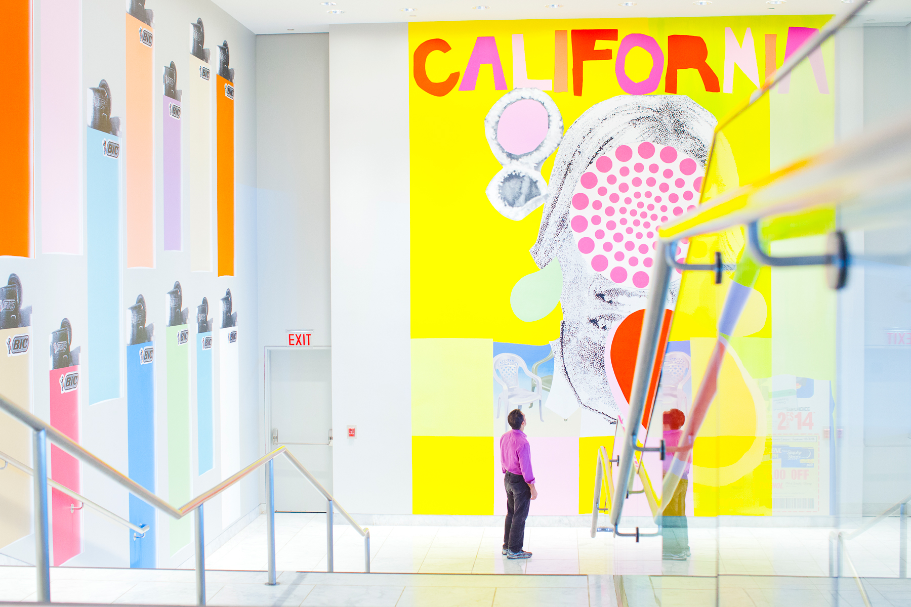 A person standing at the bottom of a stairway inside a building looking up at a mural