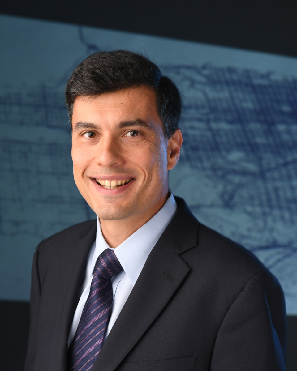 Alex Bayen smiles for a portrait wearing a business suit