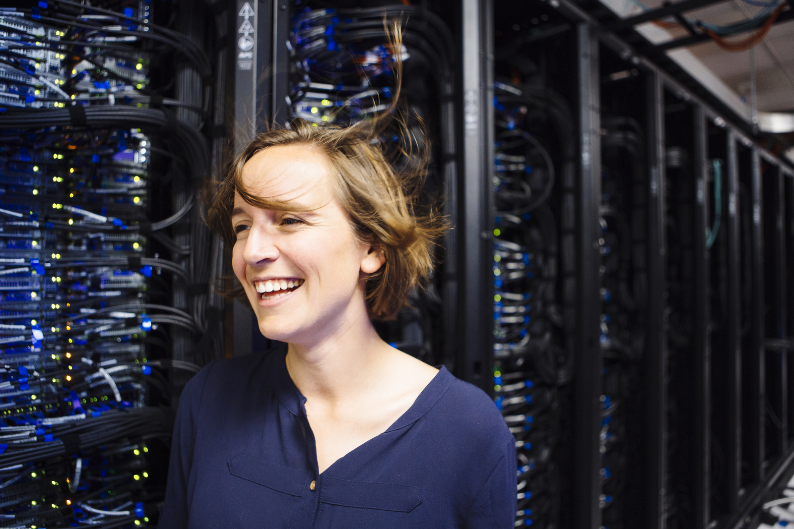Professor Molly Roberts smiles in half-profile, standing next to a server bank. Breeze from the cooling fans blows her hair askew.