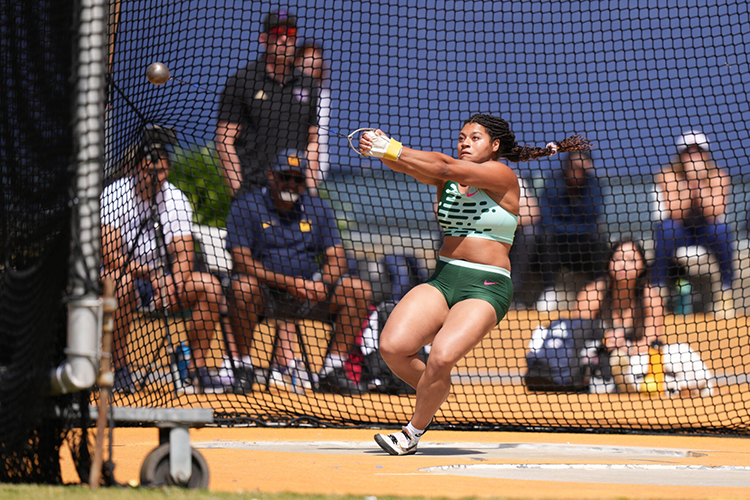 Young woman in the middle of throwing a hammer in a green uniform -- Camryn Rogers