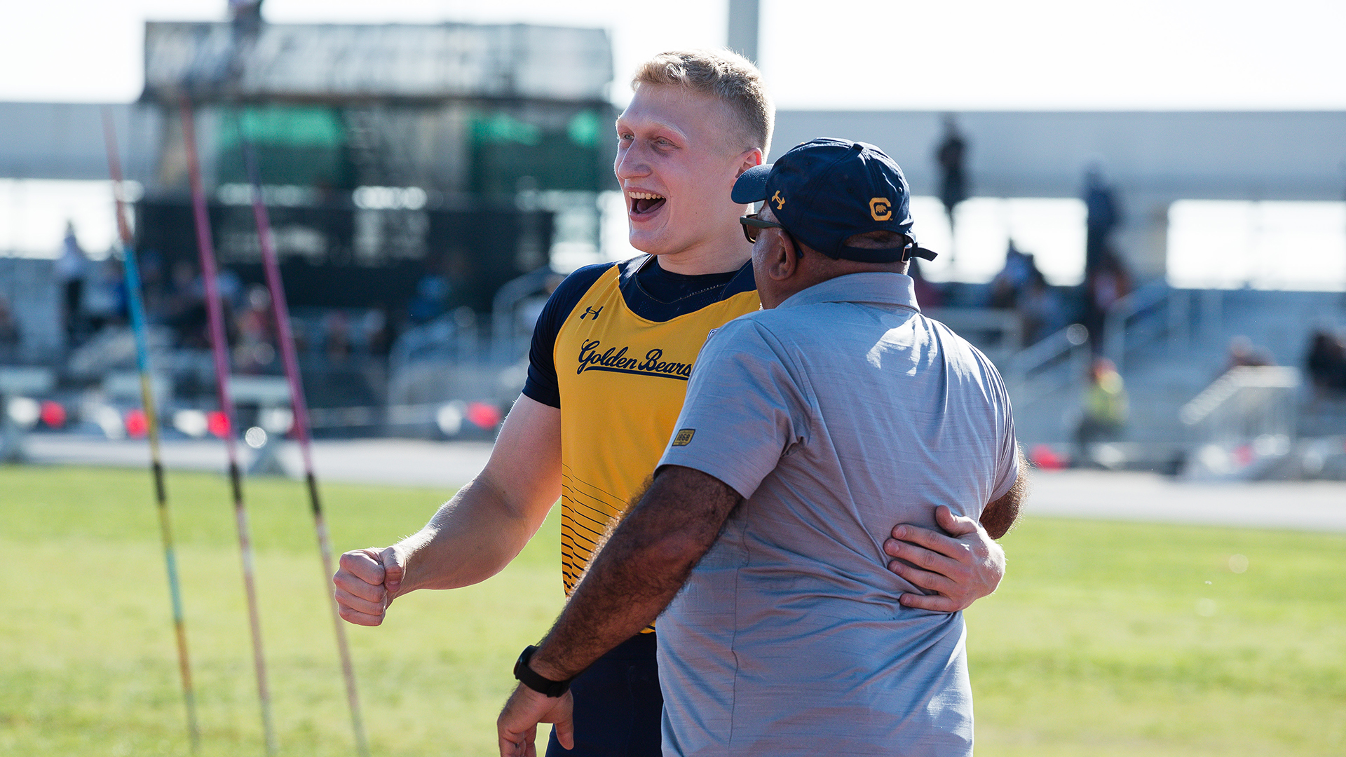 Young man with blonde hair has his arm around a stout coach as they celebrate