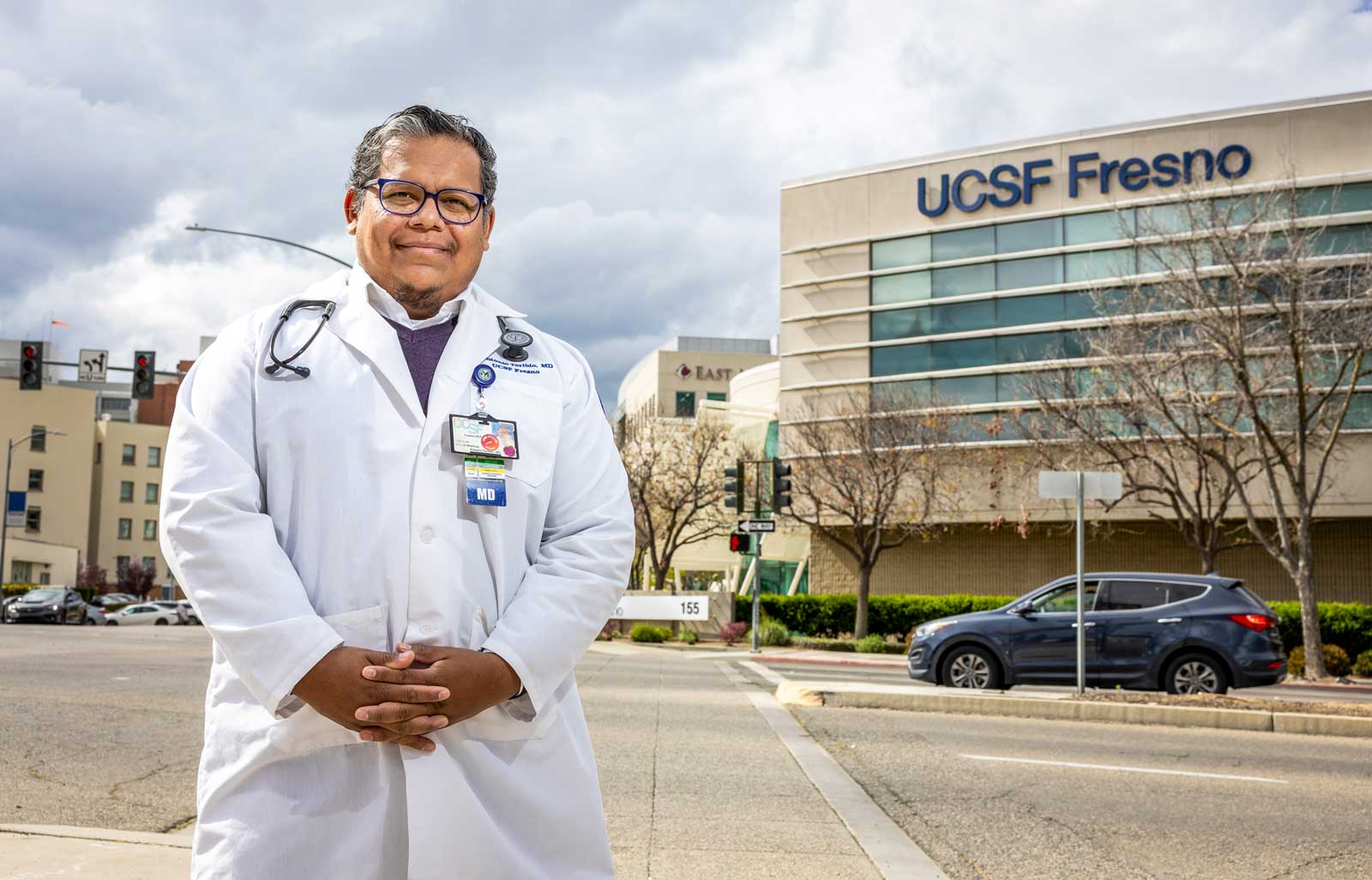Man with dark gray hair and medical coat stands on sidewalk with UCSF Fresno building behind