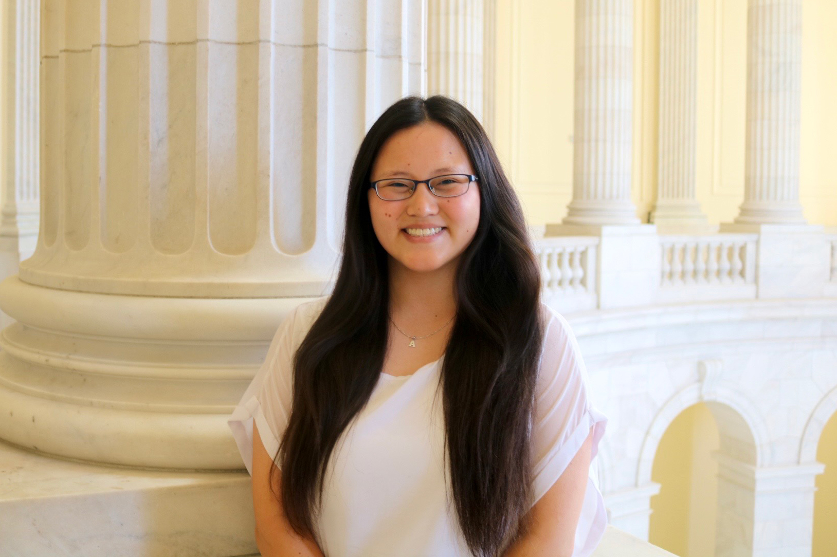 Young woman with long hair and glasses smiles at the Capitol building