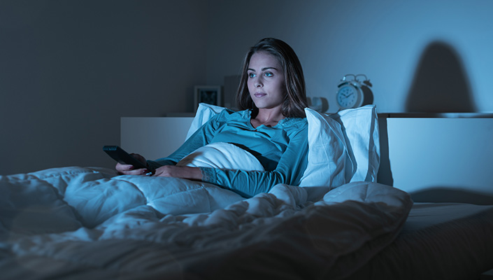 A woman sits up in bed, watching a screen