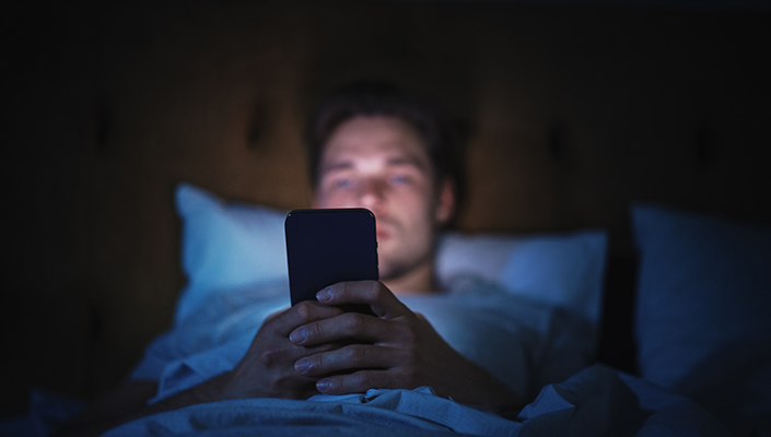 A man laying in bed looks at his phone in the dark