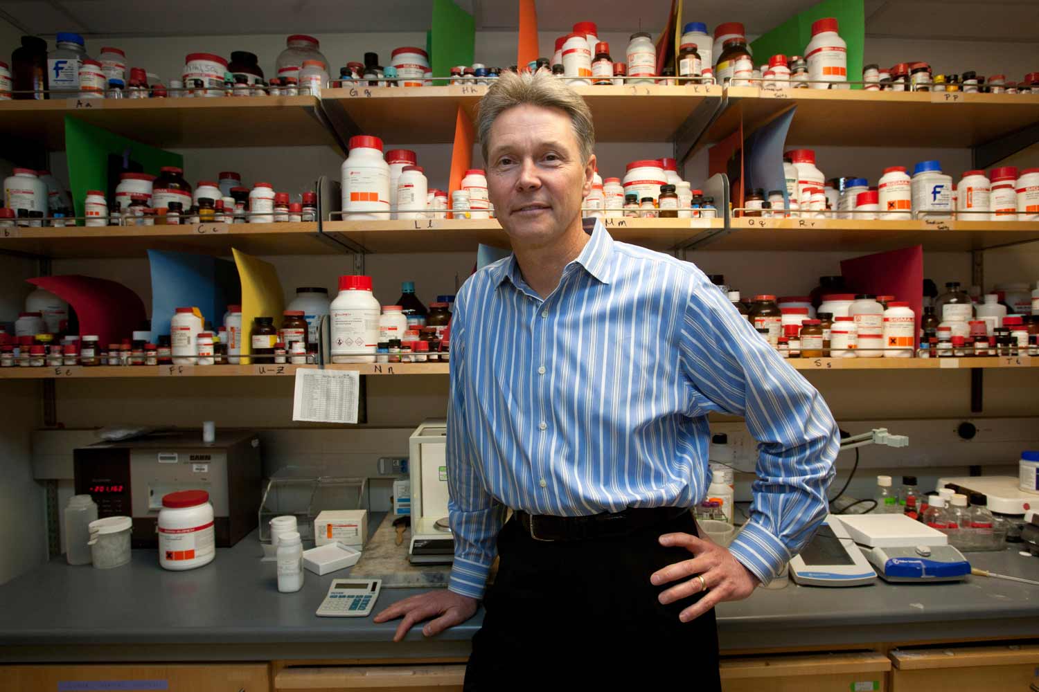 A man stands in a lab with his hand on his hip