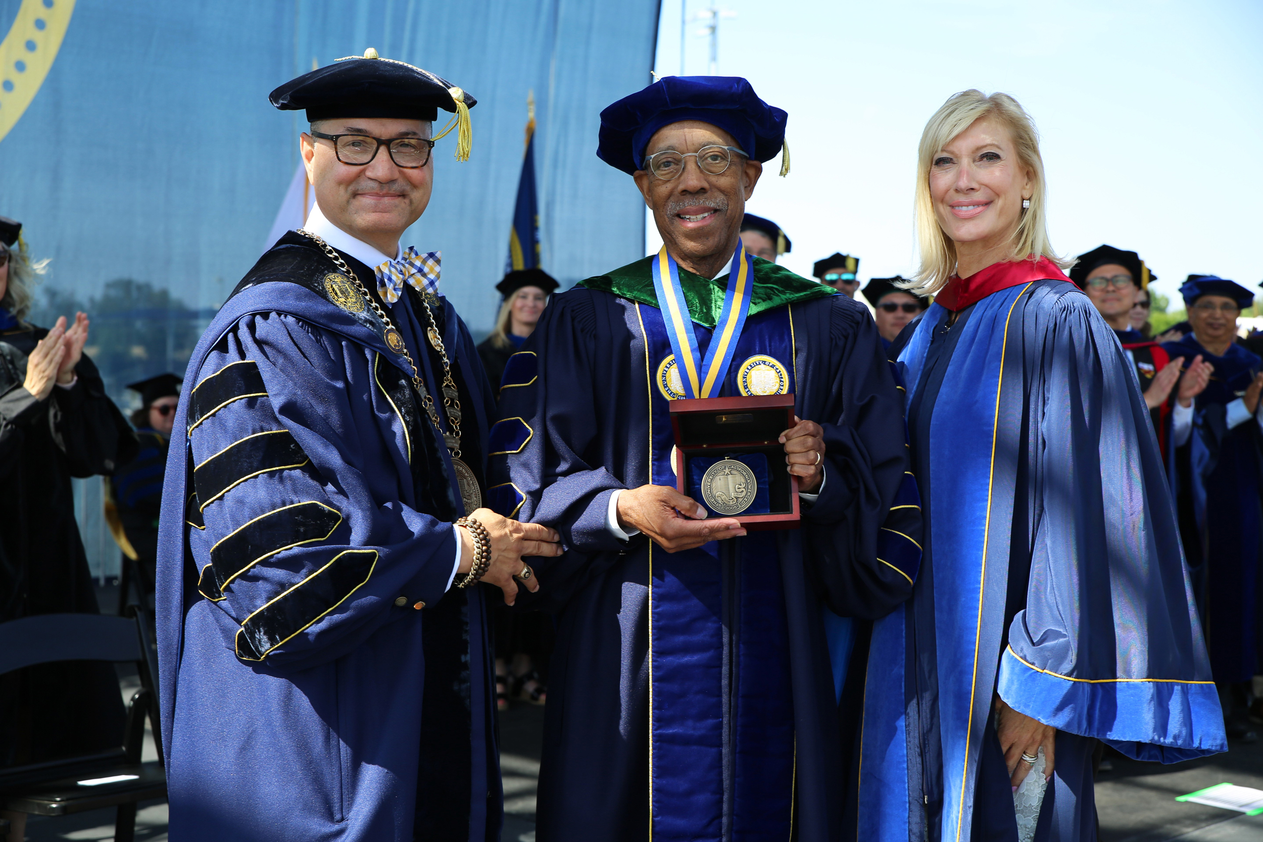 Chancellor Munoz, UC President Drake holding a medal, and Chair Janet Reilly at UC Merced's graduation in robes