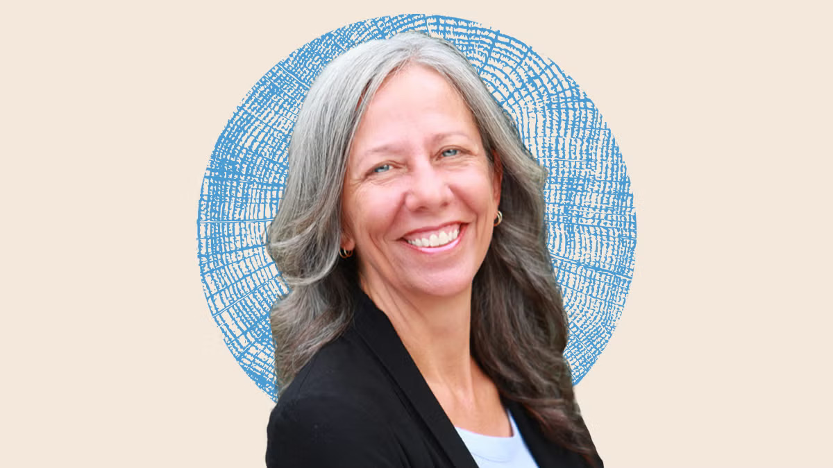 Woman with shoulder-length wavy gray hair smiling in a black jacket on an illustrated backdrop with a blue textured circle behind her