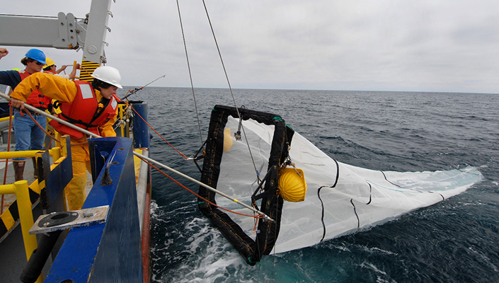 A crew on deck of a ship hauls a large net onto deck