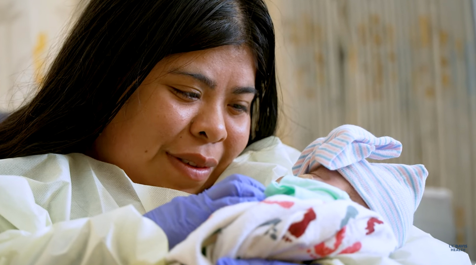 A young mother with long hair looks down at her infant she is holding in a hospital