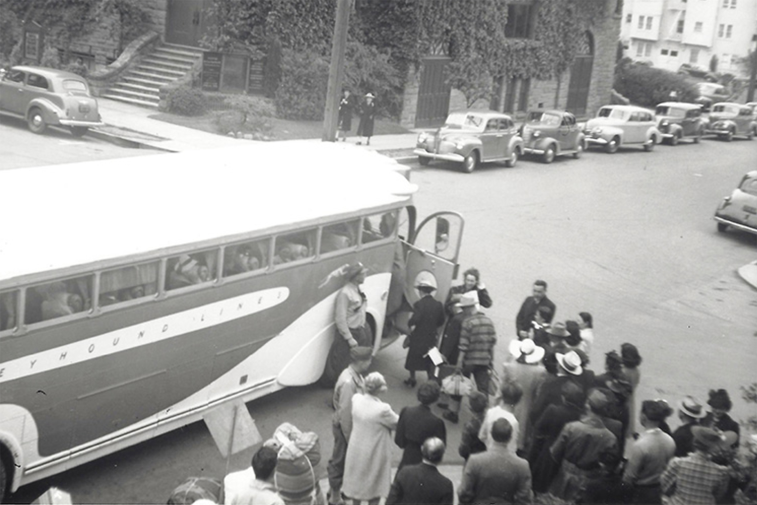 A black-and-white archival photo showing people boarding a bus dressed in coats and hats and carrying bags