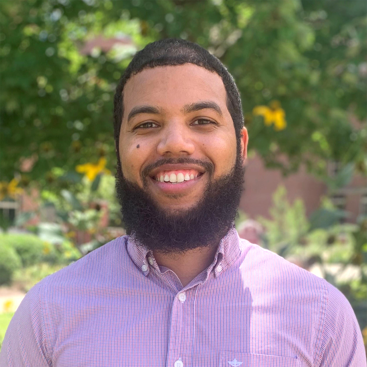 A young man with a thick beard smiles at the camera