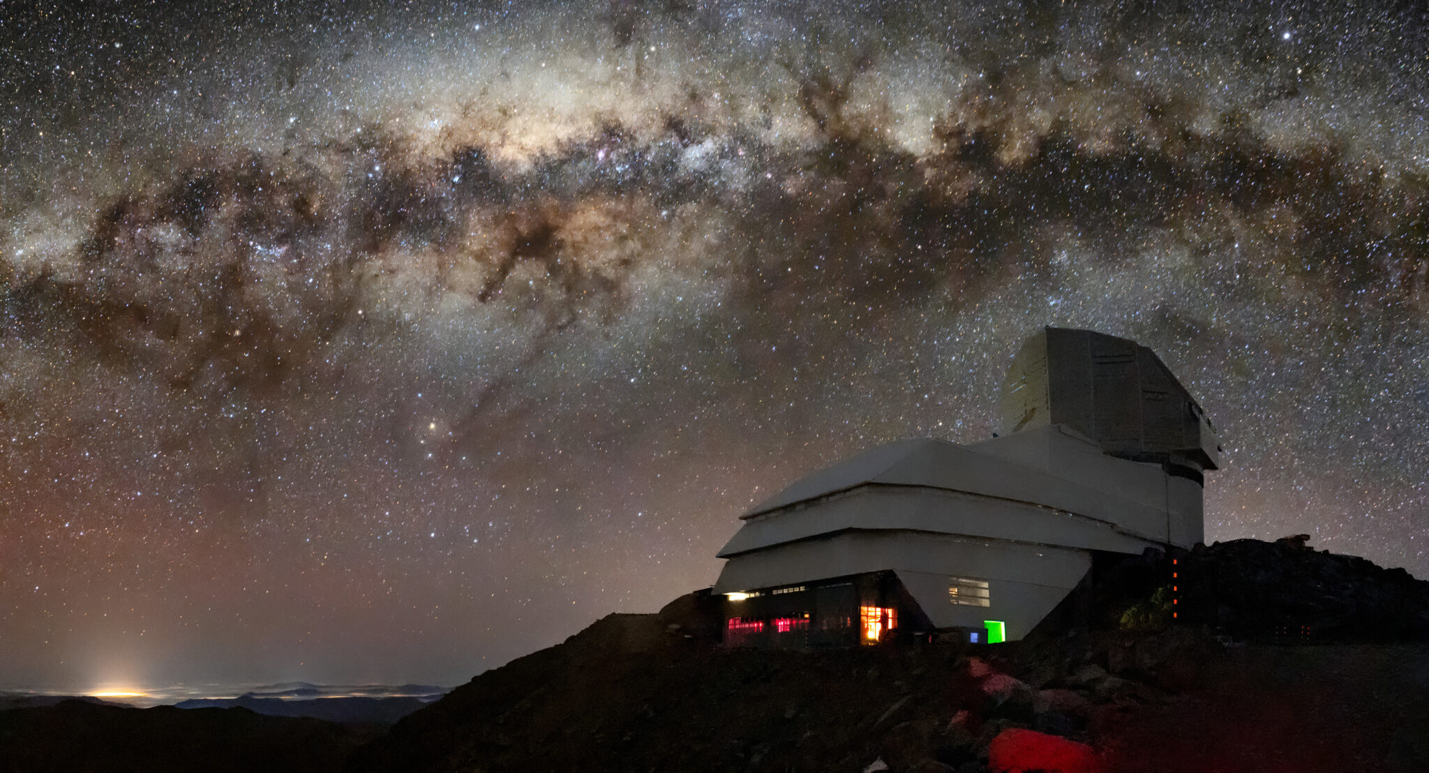 An observatory atop a mountain peak, seen at night under a dramatic, star-filled sky