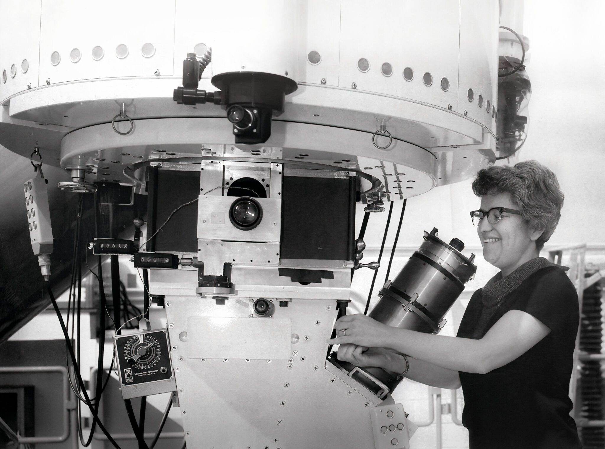 An archival black-and-white photo of a woman at a giant telescope