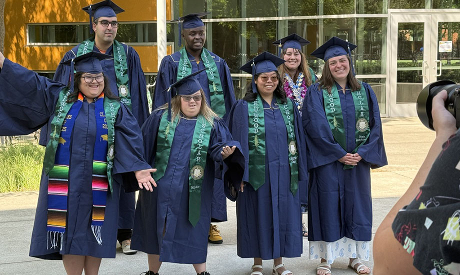 A group of students dressed in graduation regalia with caps, gowns, and Redwood Scholars stoles