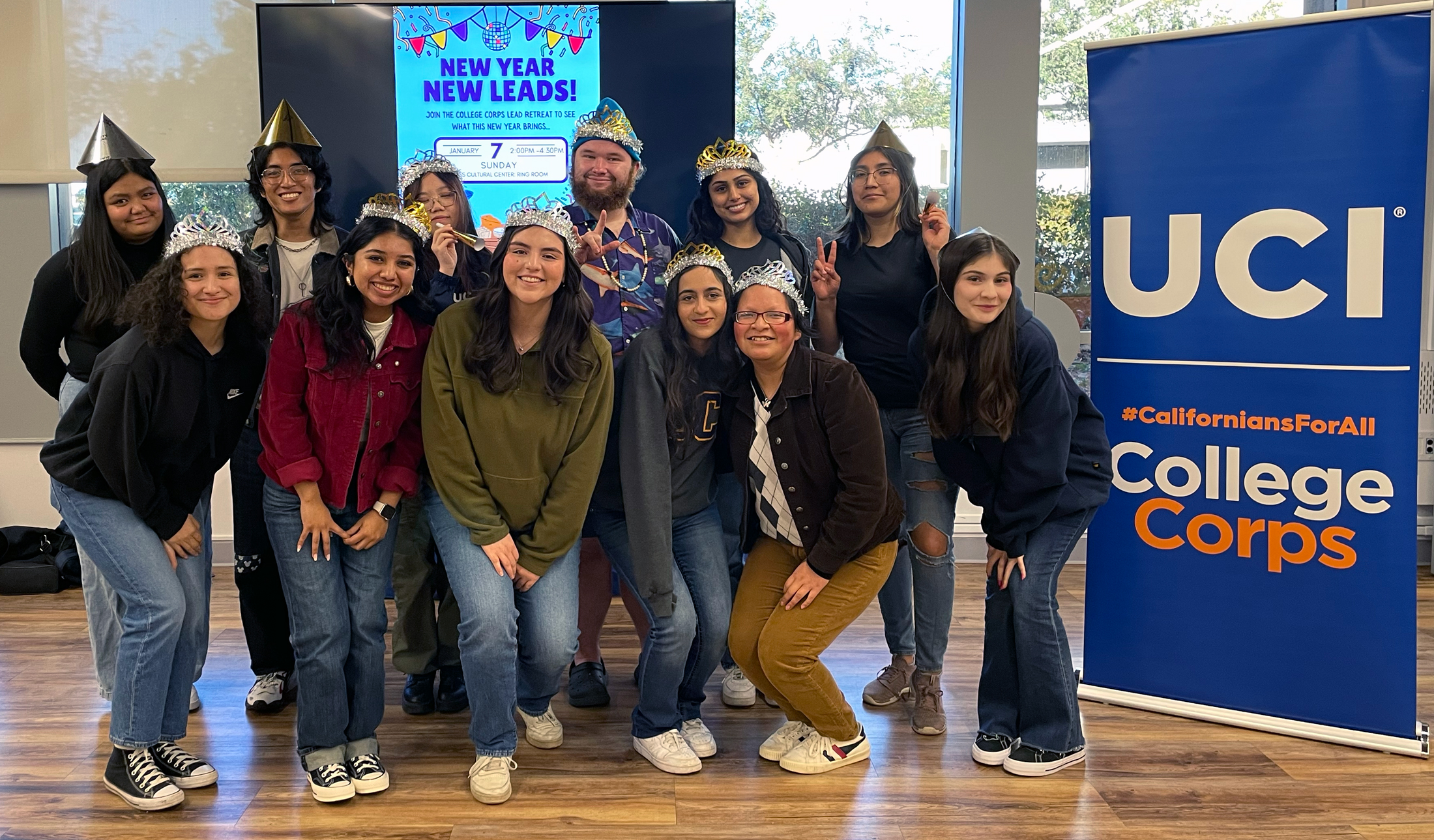 A group photo of college students in party hats with a large sign displaying UCI College Corps next to them