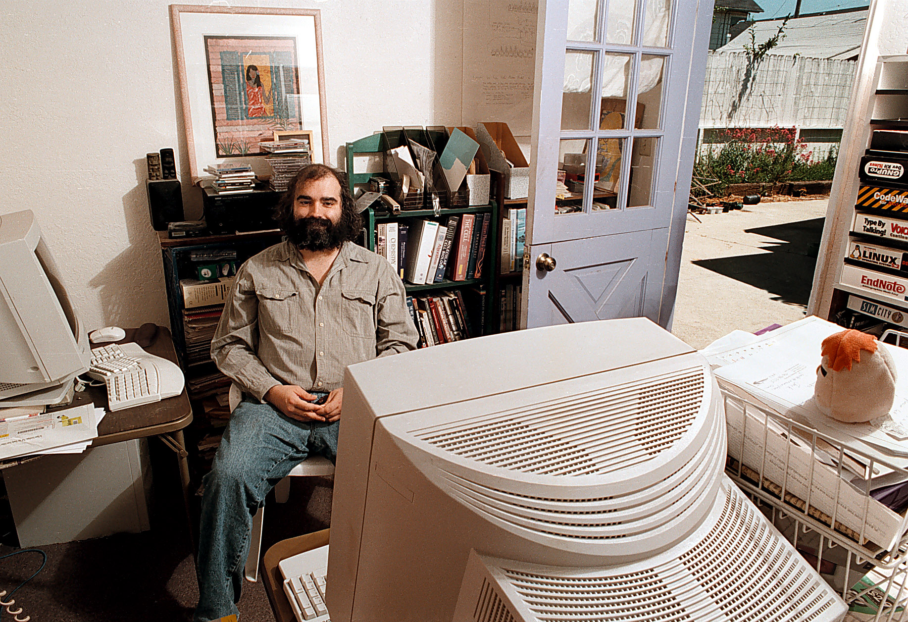 A bearded man sitting in a chair in front of two desktop computers