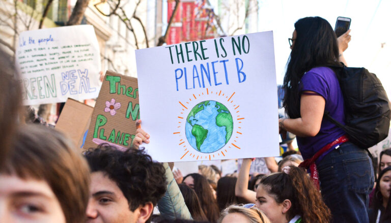 Young people at a protest, including one holding a sign reading "There is no Planet B"
