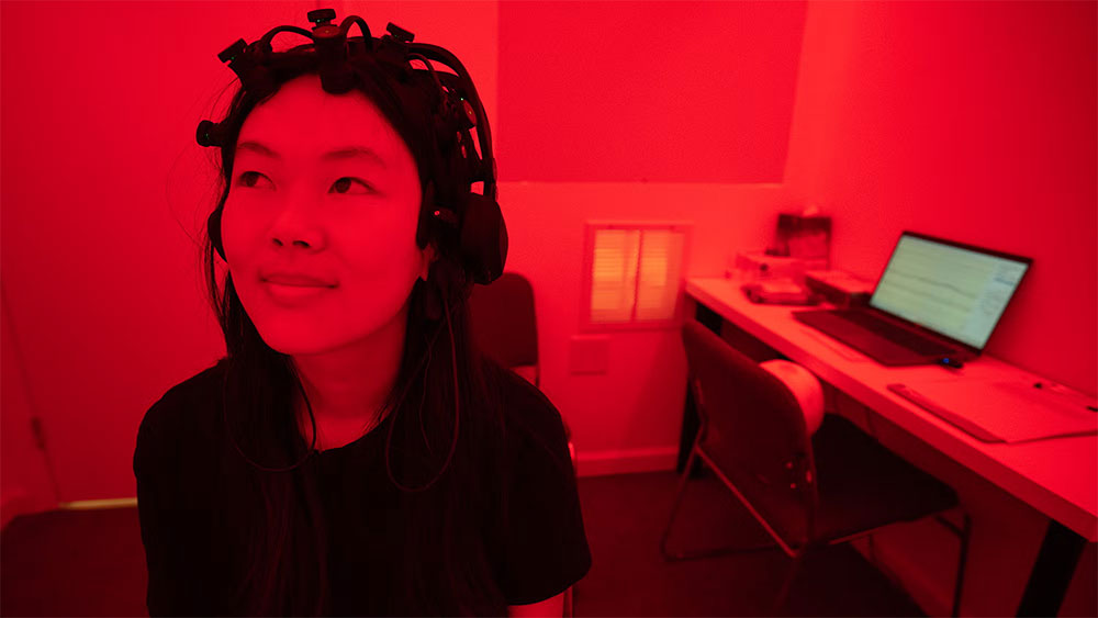 A student wearing a measuring device on her head sits in a lab bathed in red light