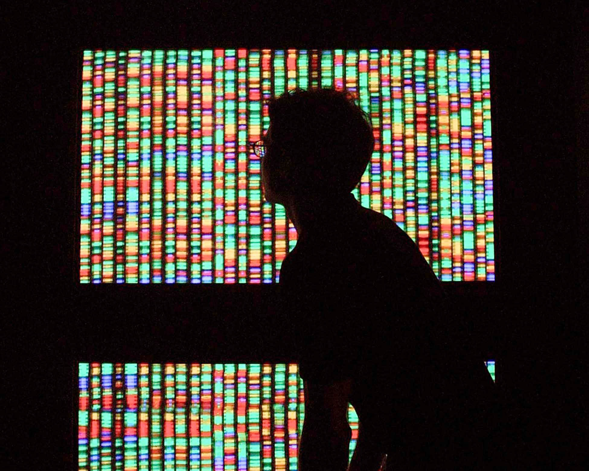 A boy looks at a lit-up wall-sized screen representing the human genome