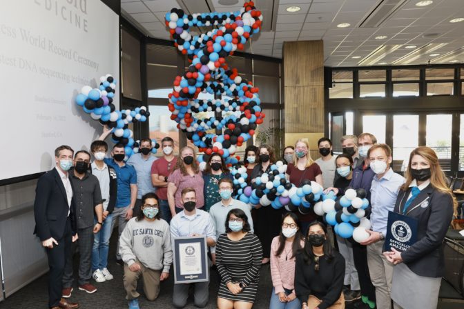 A group portrait of people wearing masks with a double helix made of balloons in the background