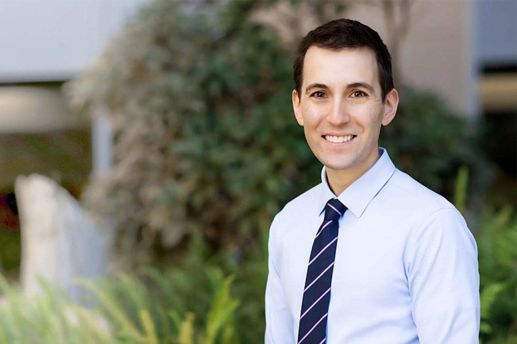 A man with a blue tie smiles outside