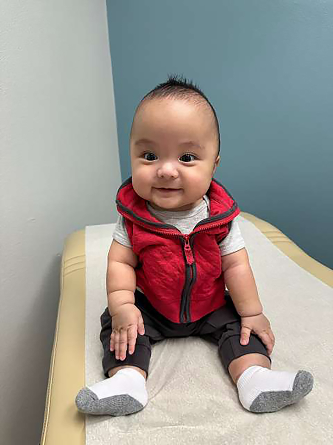 Baby Francis, sitting up and smiling at the camera on an exam bed in a doctor's office.
