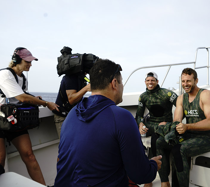 Two men are interviewed by a camera crew on a boat.