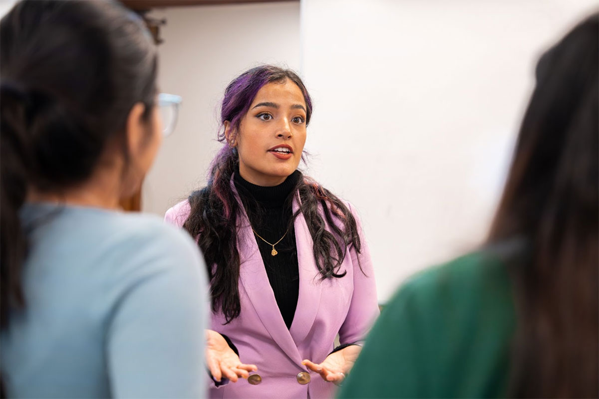 Kashish Juneja in a lavender business suit speaks to mentees