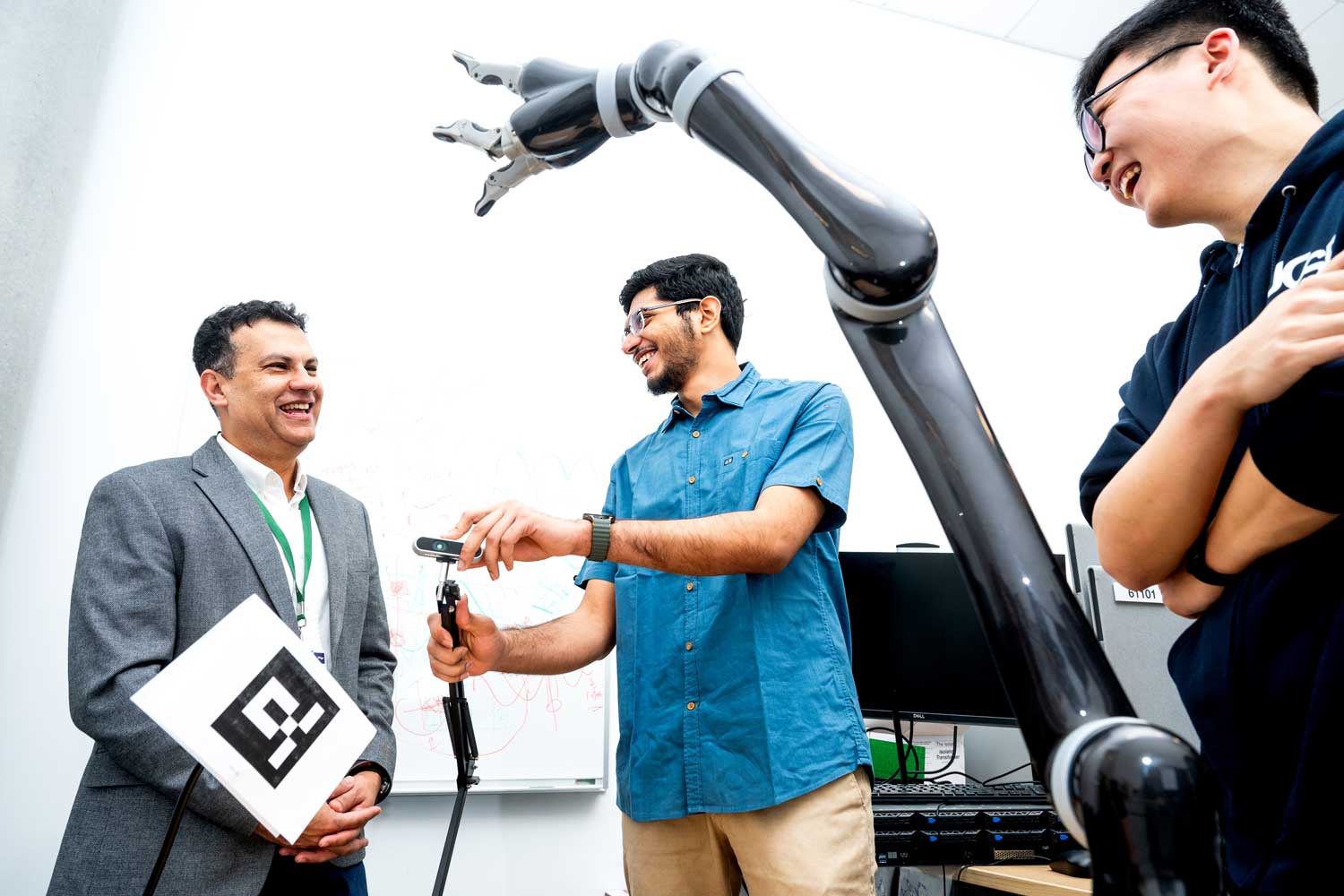 Three researchers practice using a robotic arm in a lab