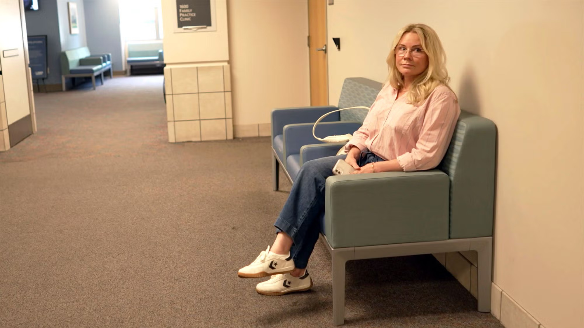 A woman sits anxiously in a hallway waiting for a doctor