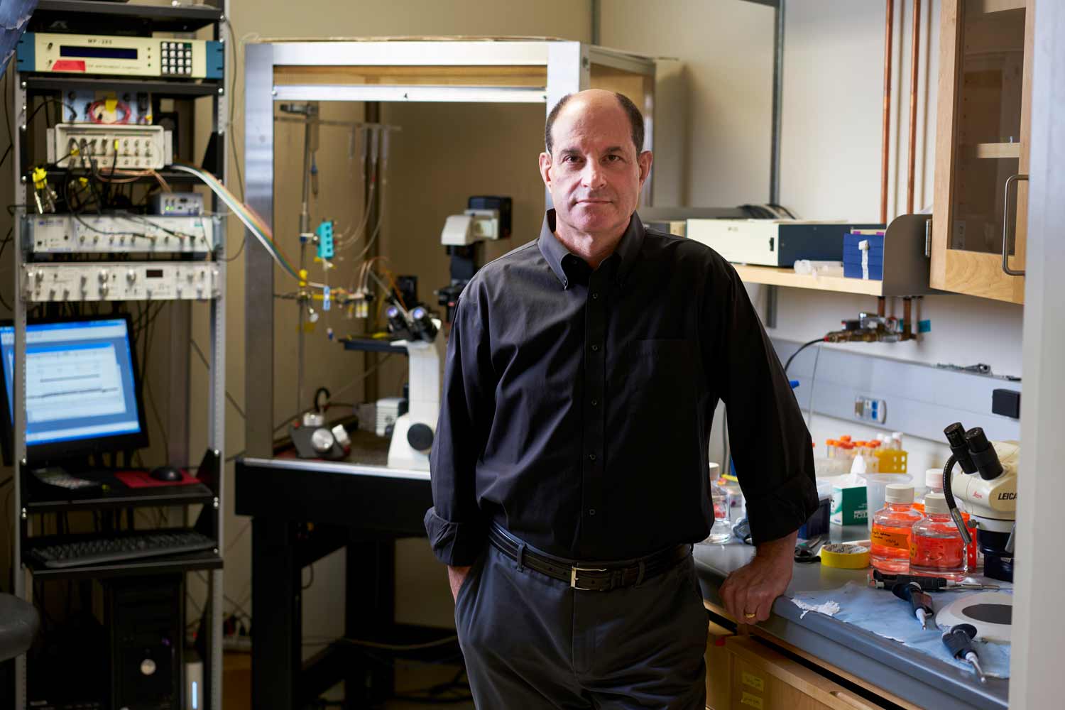 A man in a dark dress shirt stands in a lab looking at the camera