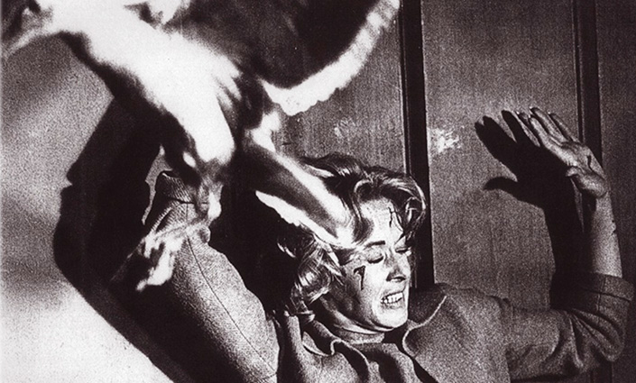 A woman acting in a horror films, arms up and disoriented after being attacked by a bird