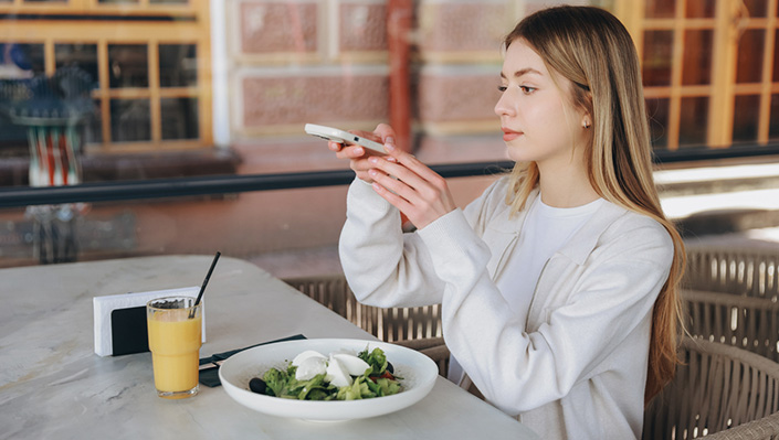 A young woman takes a picture of her plate of healthy food with a smartphone