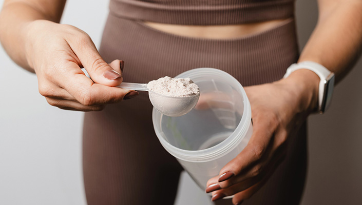A woman wearing brown matching athleisure attire scoops powder out of a plastic tub