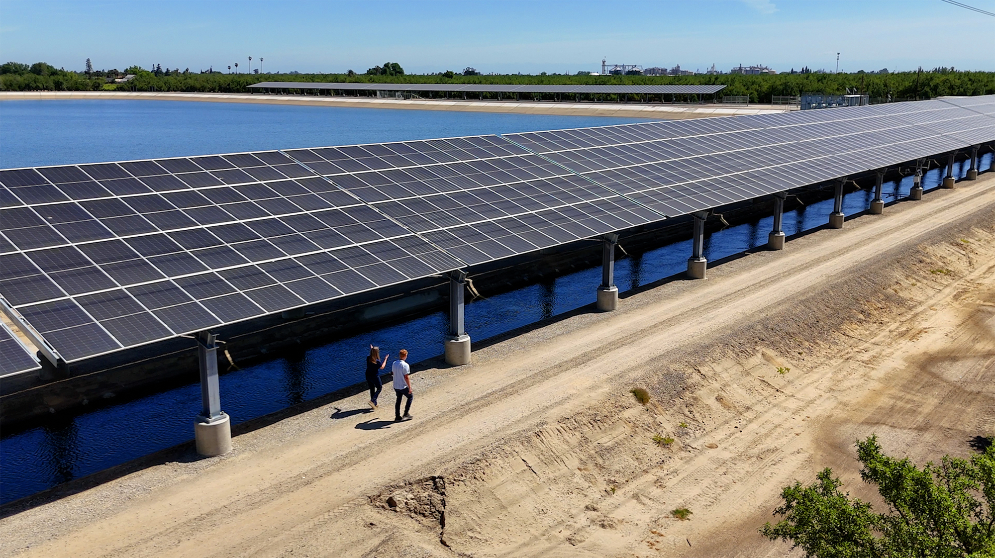 Two people walking along a series of solar panels over a canal in the Central Valley