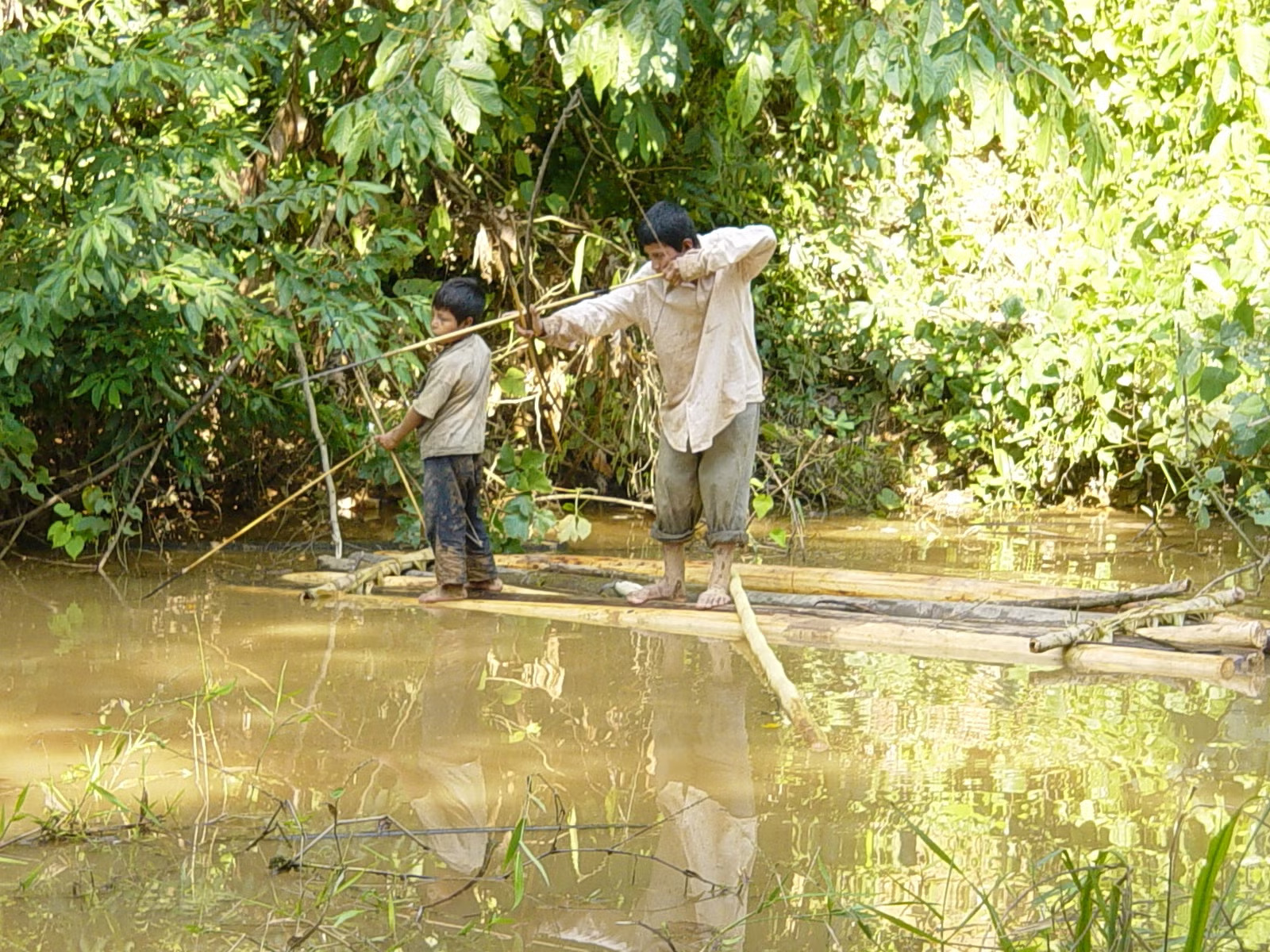 An adult and a child on a raft aim wooden bows toward the water