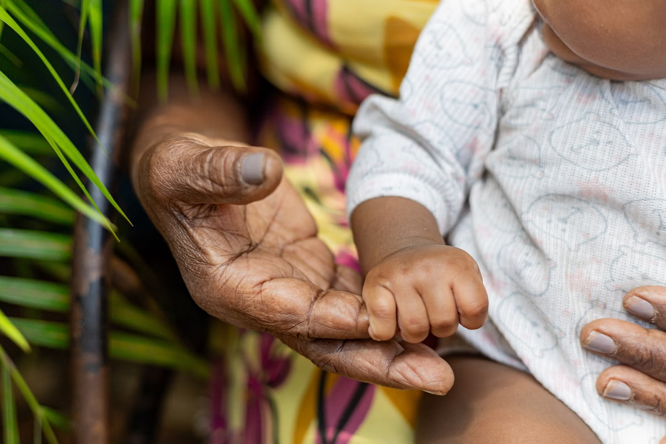 A baby holds a much larger, wrinkled hand