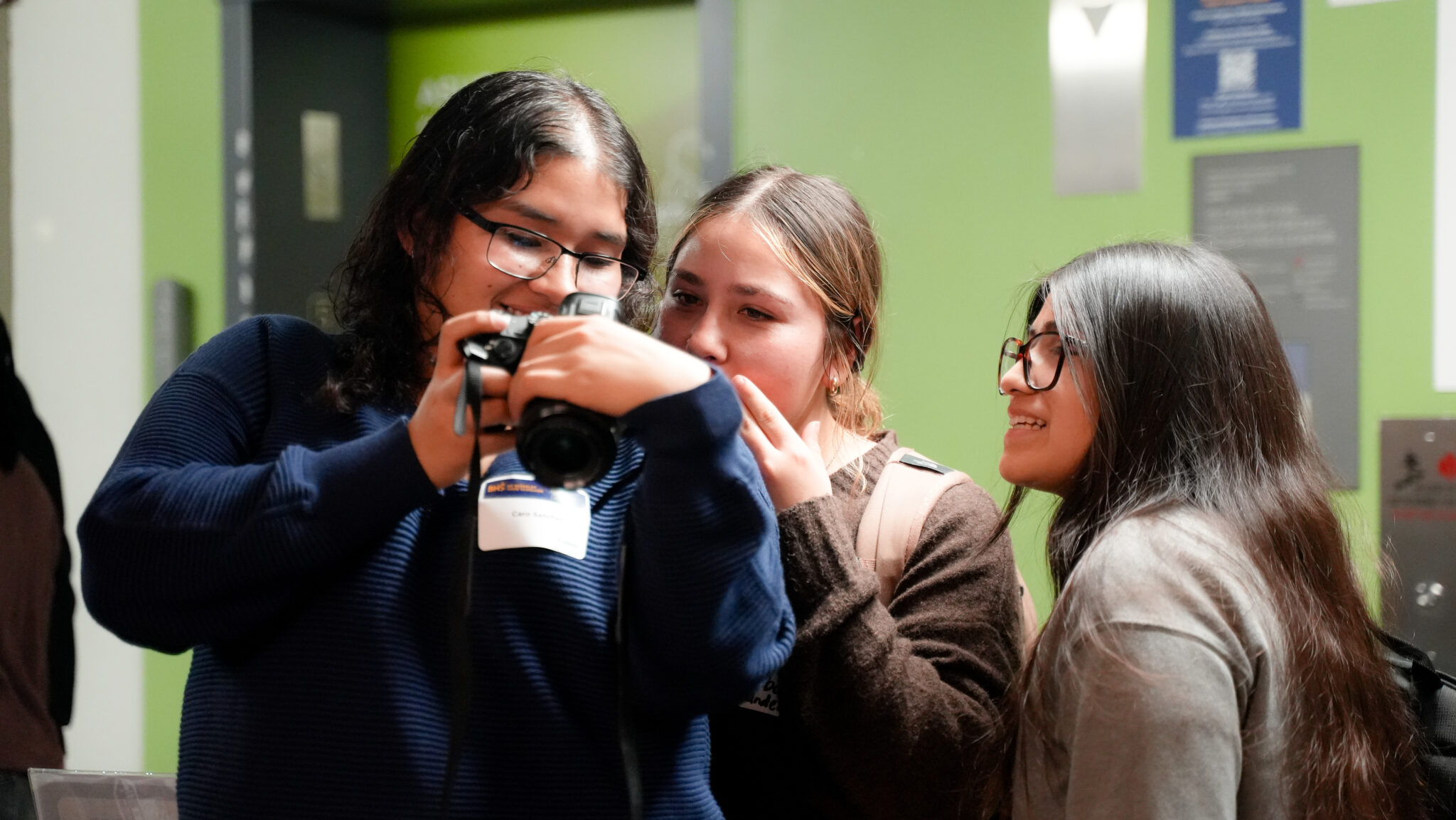Three young women look at a camera to inspect a photo