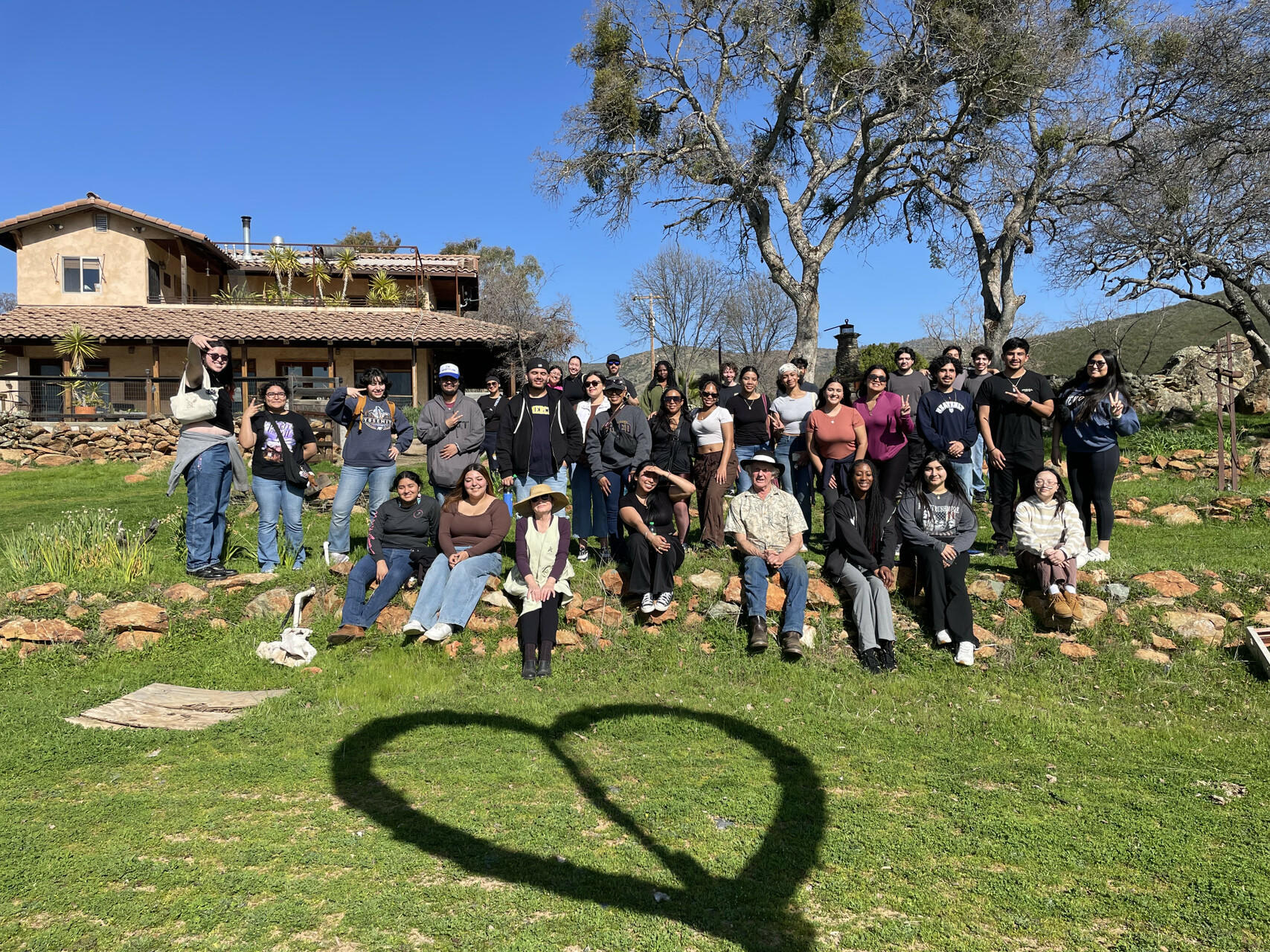 About 30 students pose for a photograph outside a home on a green lawn.
