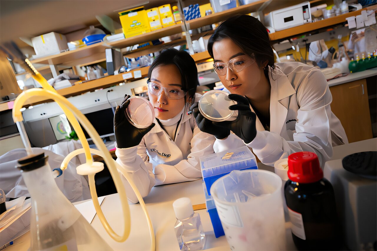 Two young women in protective gear examine something in a lab