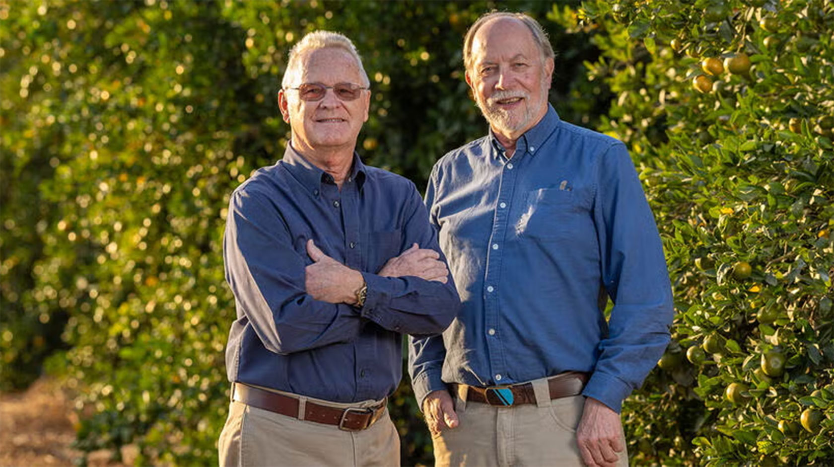 Two men in business casual smile for a phot in a citrus grove