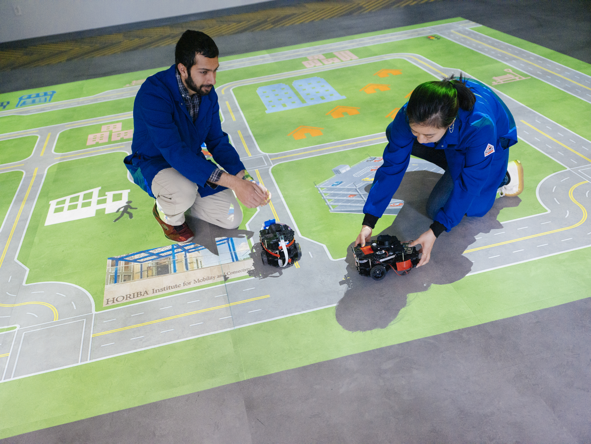 Two researchers test out small machines on a floor holding large map of urban infrastructure