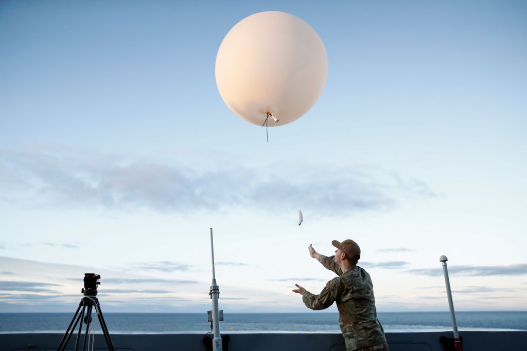A man in military fatigues releases a weather balloon from the deck of a ship