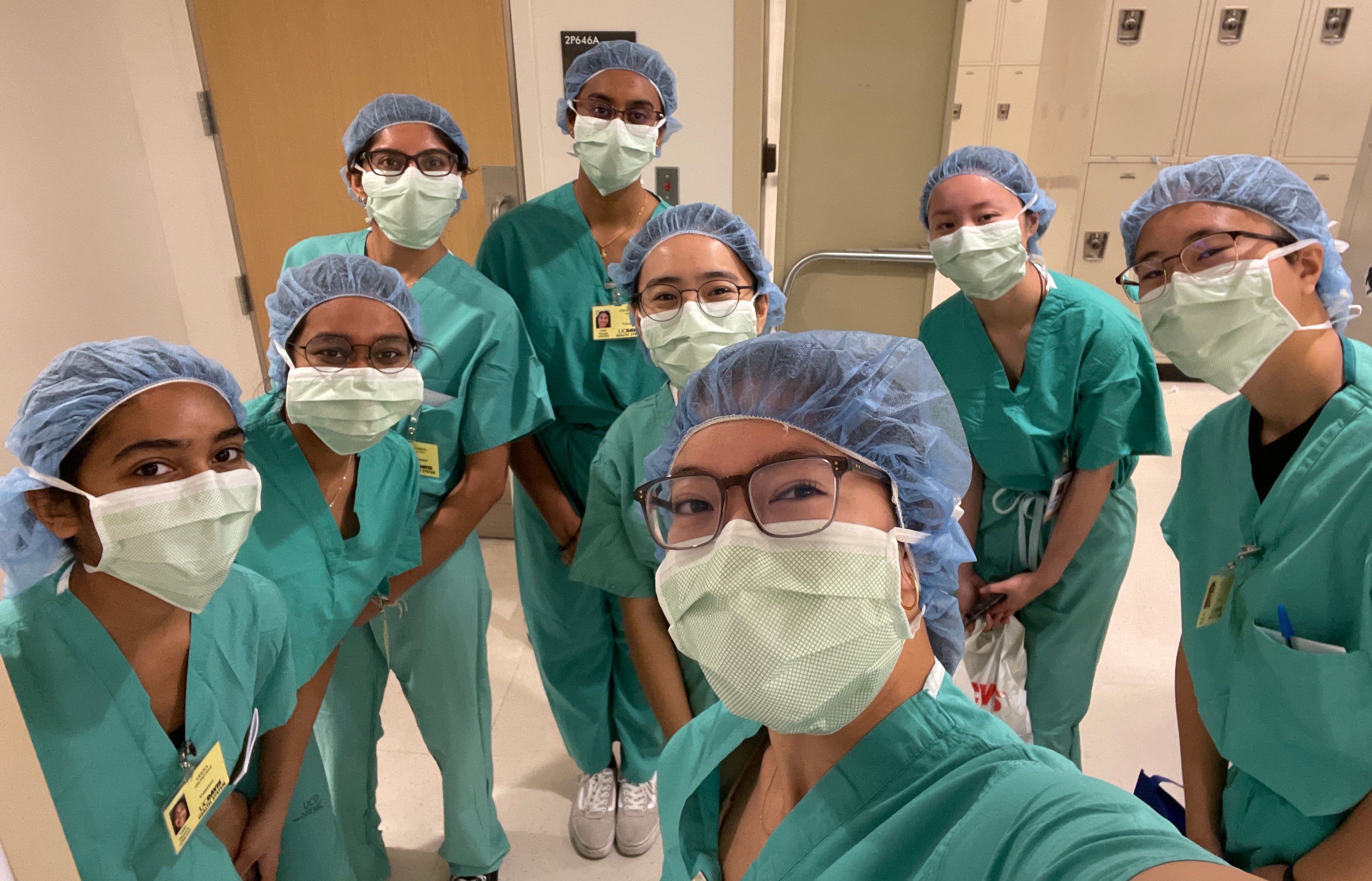 A group selfie of people wearing surgical scrubs, masks, and hair covers.