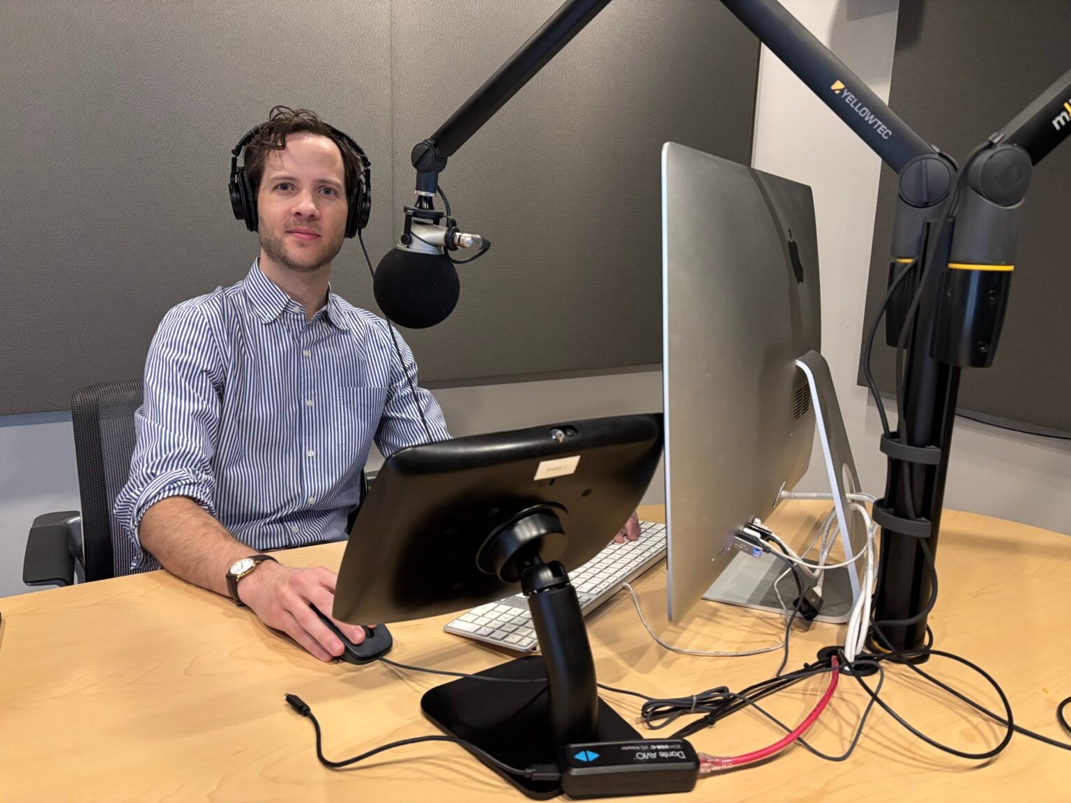 A man with headphones and a microphone in front of a computer in a podcast studio